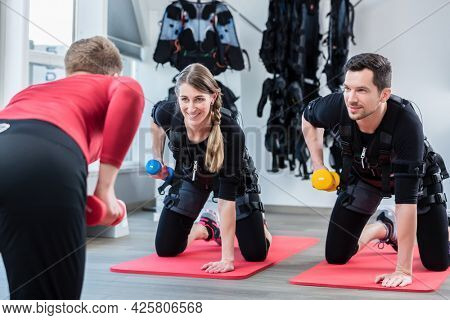 Woman and man with trainer in ems gym doing triceps exercise