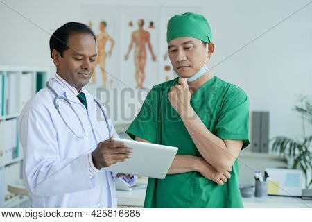 Pensive Surgeon Looking At Patients X-ray On Tablet Computer In Hands Of Chief Physician