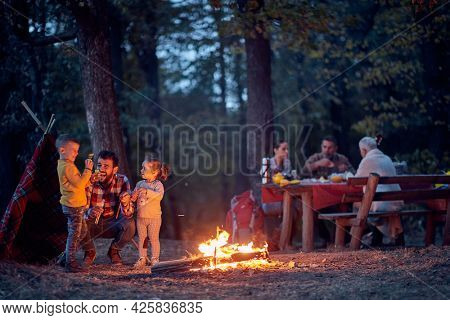 A happy family enjoying beautiful autumn dusk in the forest around a campfire