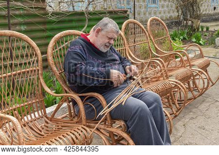 Senior Ukrainian Man Cut Sleeving While Making Whicker Rocking Chair In Summer Garden