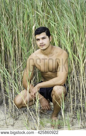 A Young Guy Is Squatting In A Reed Field And Thoughtfully Looking At You