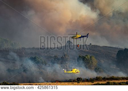 Two Helicopters, Bambi Bucket And Firefighters In The Background
