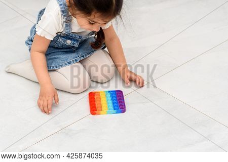Young Little Girl Sitting On The Floor At School Playing Poppit-new Fidget Toy, Popular With Kids, H