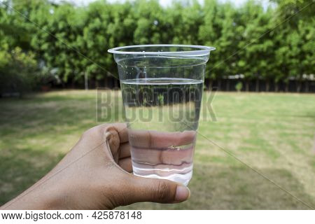 Female Holding Glass Of Clean Filtered Water In Transparent Disposable Glass At Home Garden With Bac