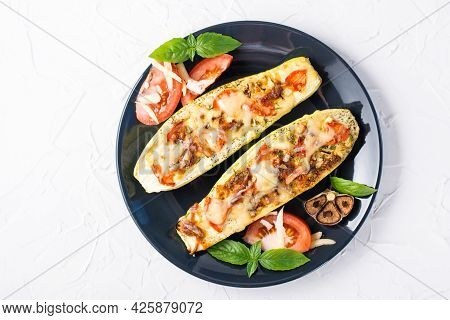 Ready-to-eat Baked Zucchini Halves Filled With Cheese And Tomato And Basil Leaves On A Black Plate O
