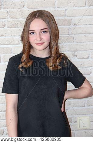 Girl With Lush Hairstyle Posing On Brick Wall Background. Portrait Of Girl In Black Dress. Hairstyle