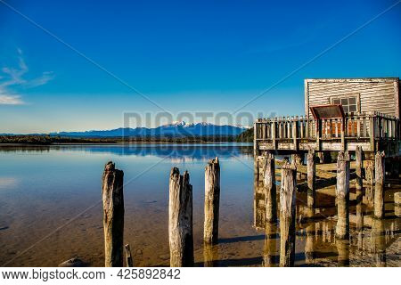 The Historic Wooden Boathouse On The Shore Of Lake Okarito With The Southern Alps In The Background