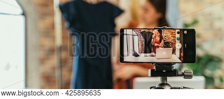Young And Beautiful Asian Woman Blogger Showing Clothes In Front Of Smartphone Camera While Recordin