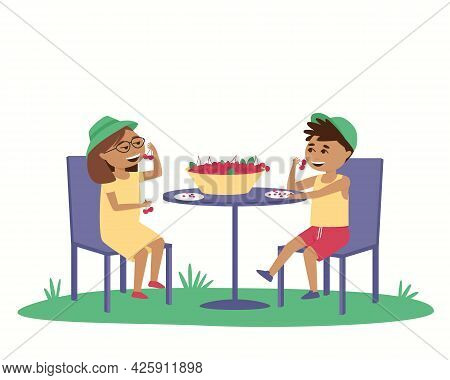 Children Eat Ripe Cherries At A Table Outside. In Summer, Children Wear Caps Outside. Isolated Boy A