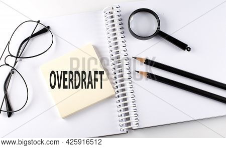 Word Overdraft On The Sicker On The Notebook With Pencils,magnifier And Glasses