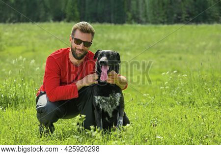 Caucasian Smiling Man, 30 Years Old, And His Happy Black Dog Are In A Countryside.