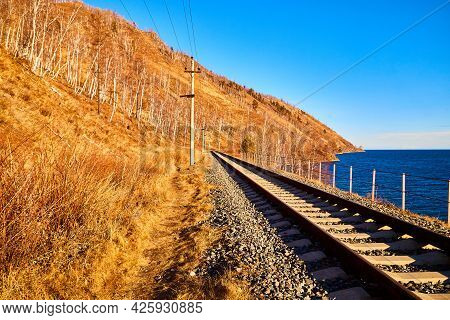 Circum Baikal Railway Running Along The Shore Of Lake Baikal On An Autumn Sunny Day With A Yellow La