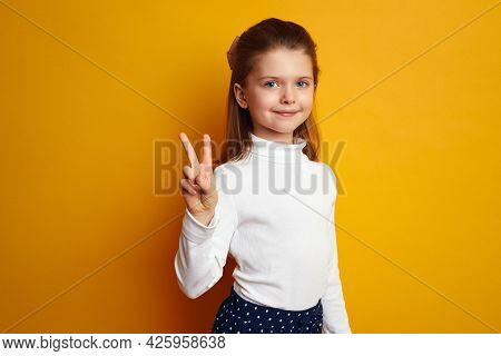 Attractive Girl Kid Showing Peace Gesture And Looking At Camera Isolated Against Bright Yellow Backg