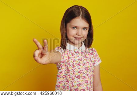 Horizontal Shot Of Adorable Little Cute Kid Girl In Stylish Clothes Smiling While Showing Peace Gest