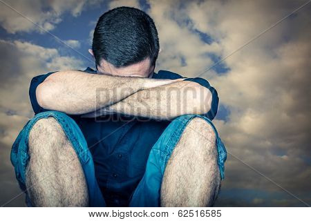 Sad young man hiding his face and crying with a stormy clouds background