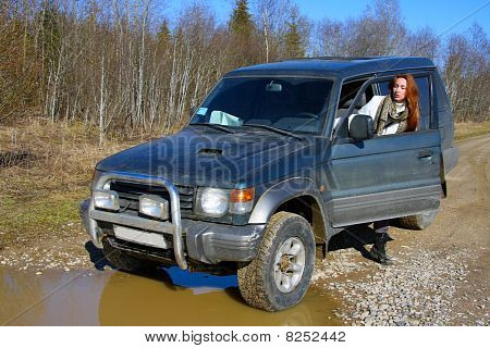 Unga kvinnan bakom rodret av offroad bil på grusväg innan vatten hinder