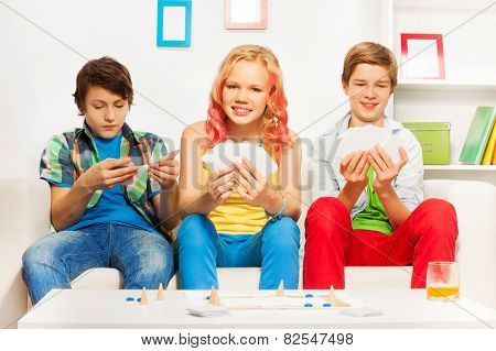 Three teenagers playing table game on white sofa