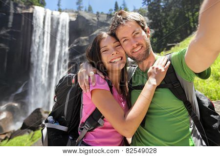 Selfie couple hikers at Yosemite National Park taking a self portrait picture with beautiful waterfall, Vernal Fall. Young hiking couple relaxing after hike in beautiful summer nature landscape.