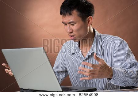 Angry business man of Chinese sitting on chair and looking at laptop on desk in studio.