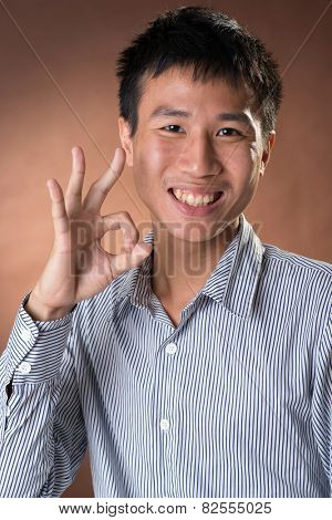 Young Chinese frank businessman give you an Okay gesture, closeup portrait in studio.