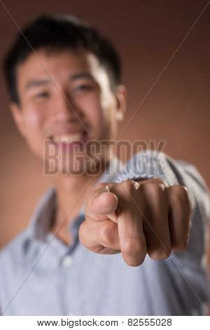 Young Chinese frank businessman point at you, focus on finger, closeup portrait in studio.