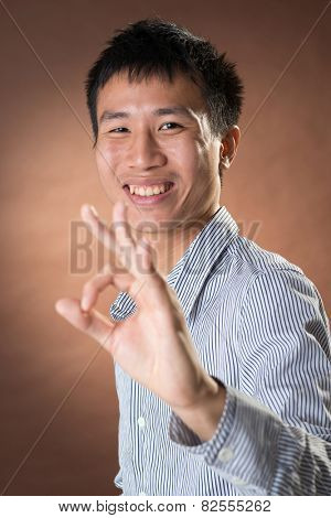 Young Chinese frank businessman give you an Okay gesture, closeup portrait in studio.