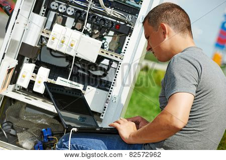 engineer working with laptop outdoors adjusting communication equipment in distribution box