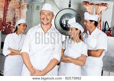 Portrait of happy mature male butcher with team in butchery
