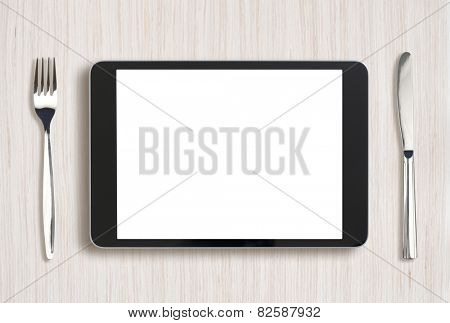 tablet pc on light wooden table with fork and knife
