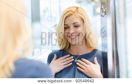 sale, consumerism, shopping and people concept - happy woman choosing and trying on pendant at jewelry store