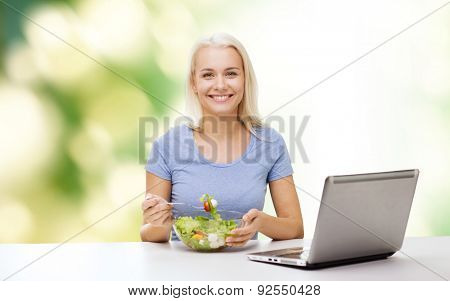 healthy eating, dieting and people concept - smiling young woman with laptop computer eating vegetable salad over green natural background