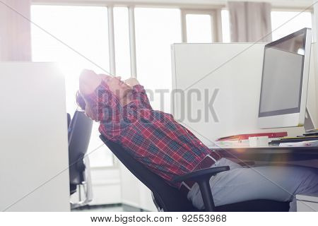 Side view of young businessman relaxing at computer desk in office