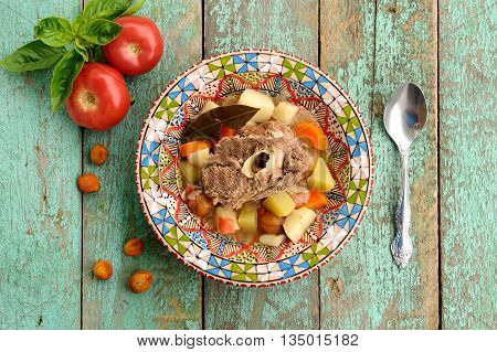 Homemade chorba soup with lamb meat on bone potato carrots bay leaf and dried apricots served with basil and tomatoes overhead view