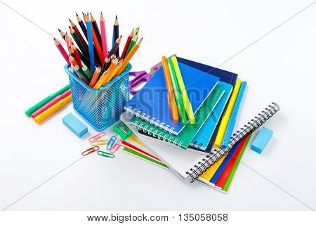 Back to school concept. Notebook and copybook stack with metal holder pencils pens paper clips sharpener and eraser on a white background