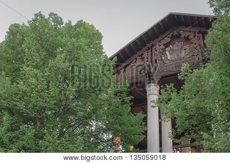 Building with columns and a wooden roof, is located behind the trees