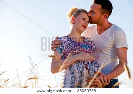 Happy and young pregnant couple hugging in nature
