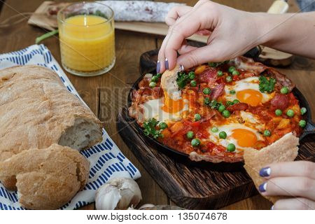 Hand dip bread into flamenco eggs or huevos a la flamenca, spanish andalusian cuisine.