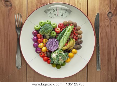 Plate with weighing scales packed with diet fruits and vegtables in a heart shape