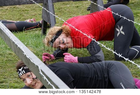 STOCKHOLM SWEDEN - MAY 14 2016: Smiling senior woman crawling below a barb wire obstacle on the grass in the obstacle race Tough Viking Event in Sweden May 14 2016