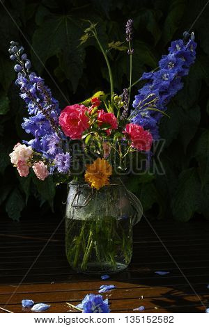 Sun after rain - colorful flowers bouquet in the garden with roses lavendel grape leaves and blue delfinium
