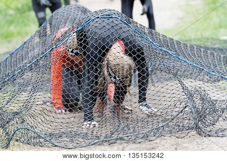 STOCKHOLM SWEDEN - MAY 14 2016: Group of women crawl under a net obstacle in the obstacle race Tough Viking Event in Sweden May 14 2016
