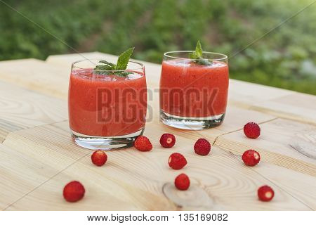 A glass of strawberry smoothie on a wooden table with mint in the garden