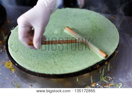 Making spinach crepe. Vegetable green crepe or pancake made by street vendor at outdoors creperie. French cuisine, cooking, commercial kitchen.