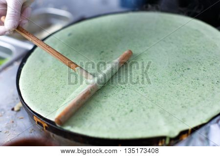 Making spinach crepe. Vegetable green crepe or pancake made by street vendor at outdoors creperie. French cuisine, cooking, commercial kitchen.