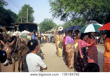 PAGAN / MYANMAR - CIRCA 1987: Women in beautiful dresses march together, two-by-two, shaded by umbrellas, in a Buddhist parade in Pagan during a holiday.