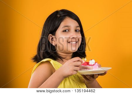 portrait of Indian kid eating cake or pastry, cute little girl eating cake, girl eating chocolate or strawberry cake over red background