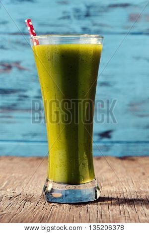 closeup of a green detox smoothie served in a glass jar with a red drinking straw patterned with white dots, on a rustic wooden surface