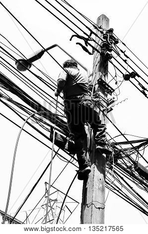 Black and White in Silhouette photo effect. Electricians repairing wire at climbing work on electric post power pole
