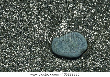 Stone flat on the shore surrounded by water on which there are numerous reflections of light