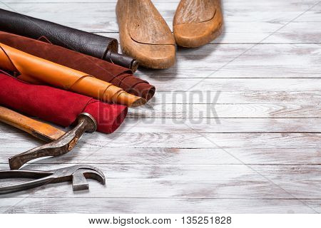 Brightly colored leather in rolls working tools and shoe lasts on the white wooden background. Leather craft. Copy space.
